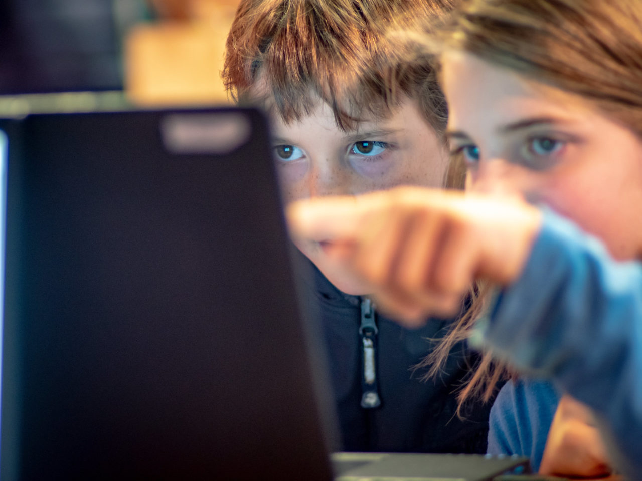 Zwei Kinder schauen konzentriert gemeinsam auf einen Laptop-Monitor