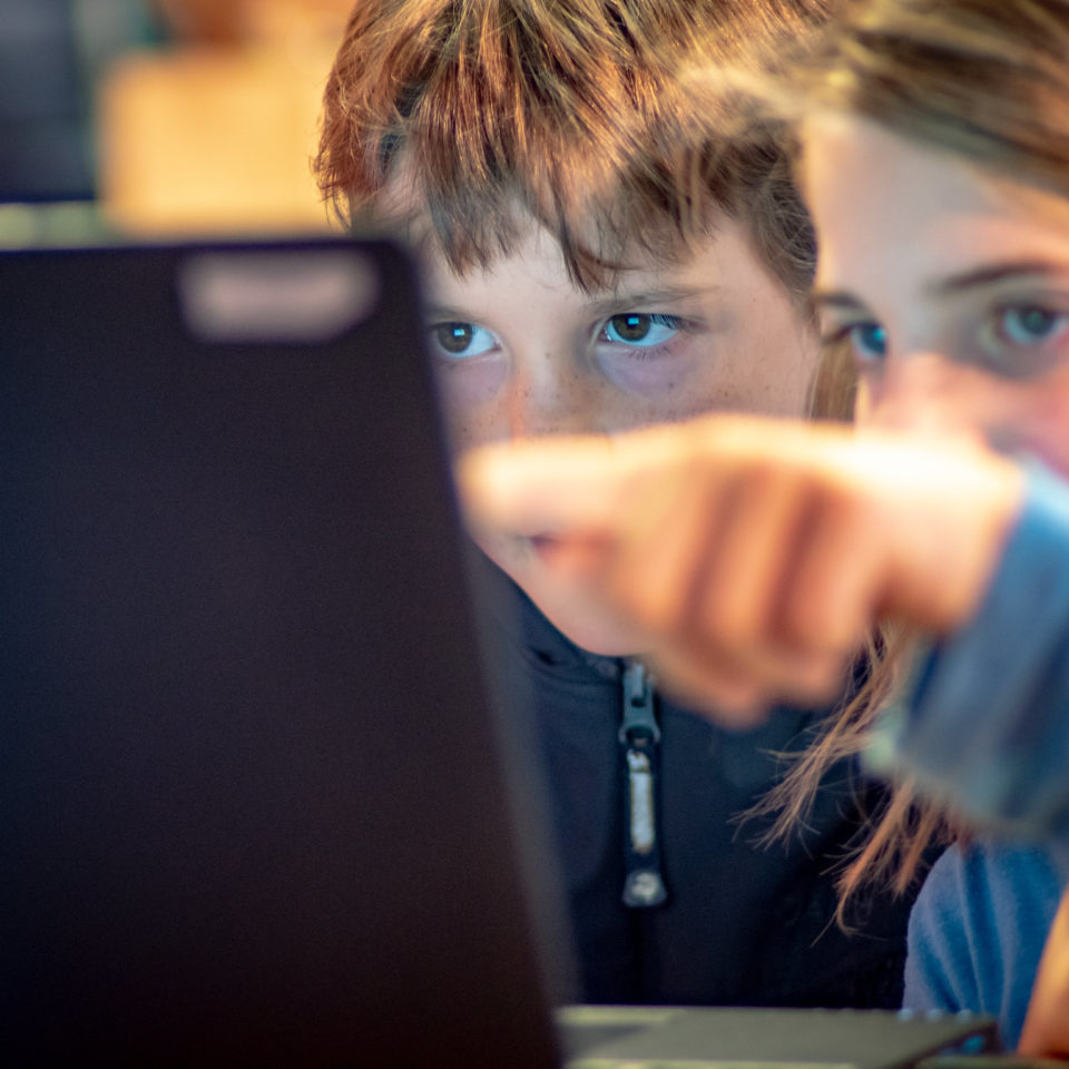 Zwei Kinder schauen konzentriert gemeinsam auf einen Laptop-Monitor